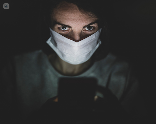 A woman wearing a covid-19 face masks looks up to the camera.