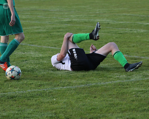 Footballer lying on a pitch in pain, after receiving a knee injury.