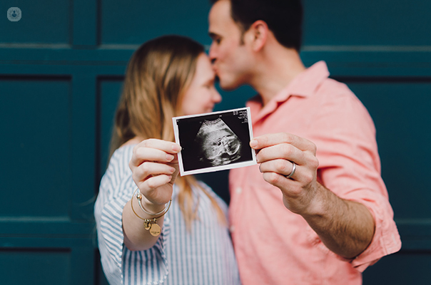 Man and woman kissing holding a pregnancy ultrasound picture.
