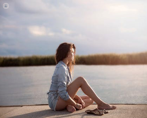 Woman sitting by lake. Some women experience reccurent UTIs, which the Uromune vaccine system can help treat.