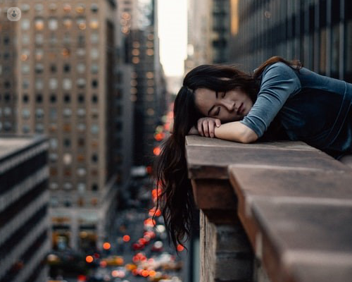 Tired woman resting on a balcony wall in a busy city