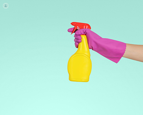 Hand in plastic cleaning glove holding bottle of spray