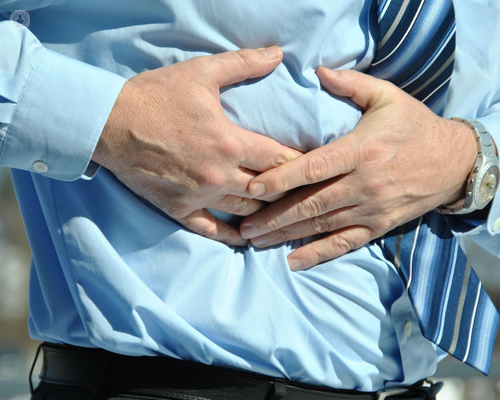 Close up of a businessman's stomach area, which he's holding due to a gastric ulcer