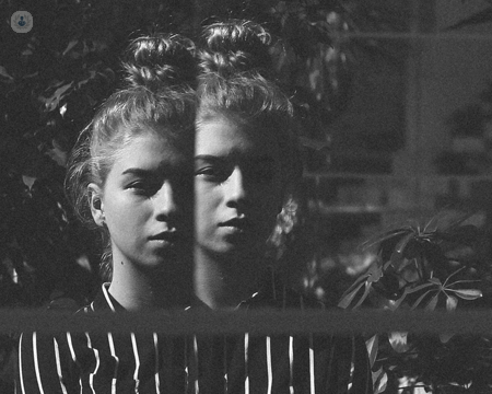 Girl with possible psychotic disorder looking into mirror with a double reflection