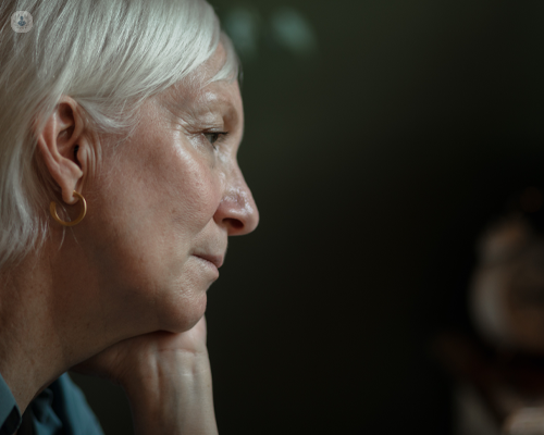 Older woman with grey hair, looking concerned against a black background