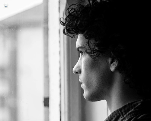 A black and white image of a man looking out a window with a pensive expression.