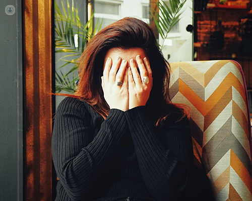 A person covering their face with their hands in despair as they suffer with a migraine