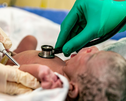 Newborn baby yawning while a doctor is listening to their heart with a stethoscope.