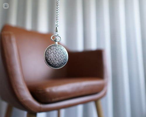 Empty brown leather chair and intricate pendant set against a white curtain