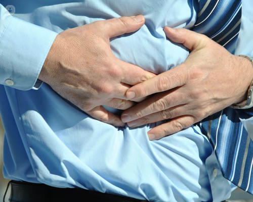 Close up of a torso of a man wearing a blue shirt, holding the side of his stomach