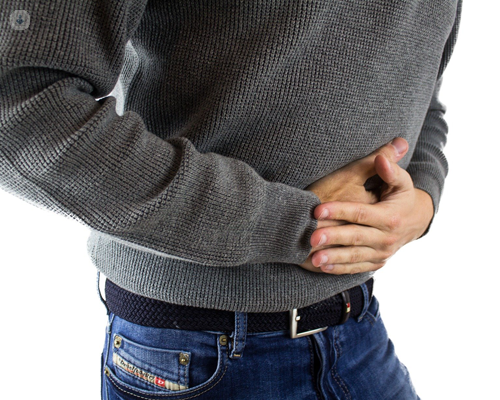 Man wearing grey jumper and blue jeans holding stomach
